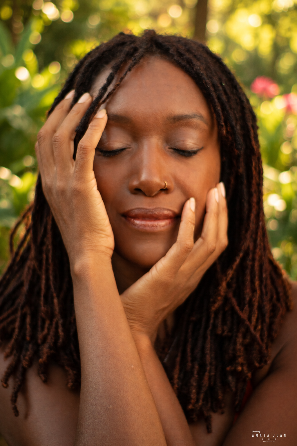 Whitsa with eyes closed and hands resting on her face, against a sunlit garden background